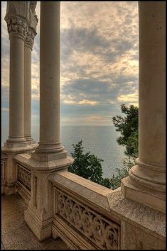 an old building with columns and pillars overlooking the ocean on a cloudy day at sunset