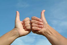 two hands making the middle finger sign against a blue sky with clouds in the background