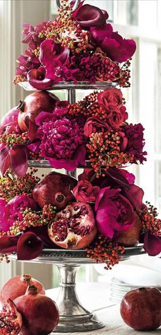 a three tiered cake with pomegranates and flowers on it, sitting on a table