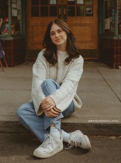 a woman is sitting on the curb in front of a building with her legs crossed