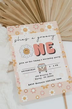 a pink birthday party card with a flower on it and a wooden fan behind it