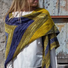 a woman wearing a yellow and blue knitted shawl standing in front of a wooden door