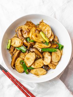 a white bowl filled with stir fry vegetables and chopsticks on top of a table