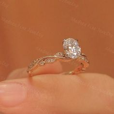 a woman's hand holding a ring with a diamond in the center and an intricate band around it