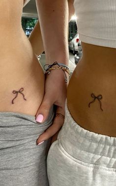 two women with small tattoos on their stomachs, one is holding the other's back