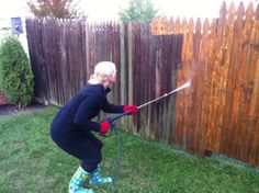 a woman is spraying water on a fence with a sprayer in her hand and wearing rubber boots