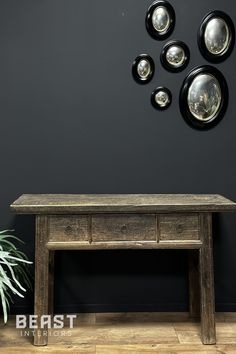 a wooden table sitting in front of a black wall with plates hanging on the wall