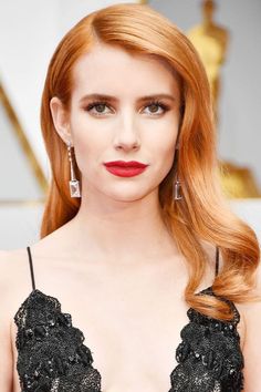 a woman with long red hair and black dress on the oscars red carpet, looking at the camera