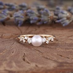 a pearl and diamond ring sitting on top of a piece of wood with lavender flowers in the background