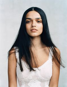 a woman with long black hair wearing a white dress and holding her hands in her pockets