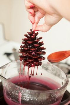 a pine cone is being dipped with red liquid in a bowl on the stovetop