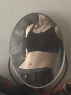 a woman's reflection in a mirror shows her stomach and waist, while wearing black shorts