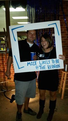 a man and woman standing next to each other in front of a brick wall holding a sign