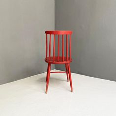 a red chair sitting on top of a white floor next to a gray wall in an empty room