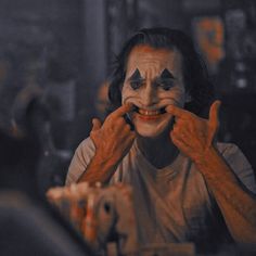 a man with clown makeup holding his hands up to his face