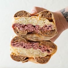 a hand holding a sandwich with meat and cheese on it's buns in front of a white background