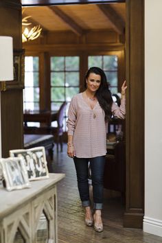 a woman standing in the doorway of a house with her hand up and smiling at the camera