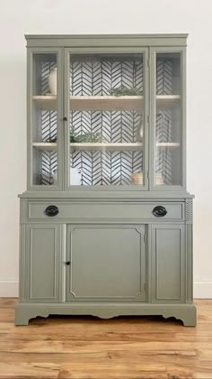 a green china cabinet with glass doors and shelves on the top, in front of a white wall