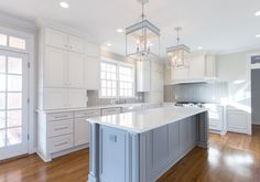 a large white kitchen with an island in the middle and two pendant lights hanging from the ceiling