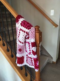 a red and white crocheted blanket sitting on top of a wooden banister