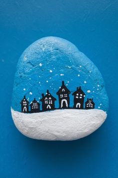 a painted rock with houses on it against a blue background that has snow falling off the rocks