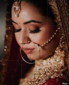 a woman in a red and gold bridal outfit with pearls on her head, nose ring