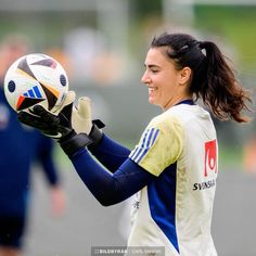 a woman holding a soccer ball in her right hand and wearing gloves on the other side