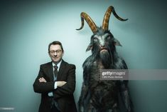 a man standing next to a goat with horns on it's head and his arms crossed