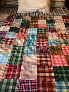 an unmade bed covered in multicolored plaid sheets and pillowcases with pillows on each side