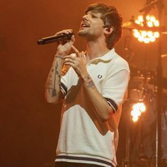 a man standing on top of a stage holding a microphone in his hand and wearing a white shirt