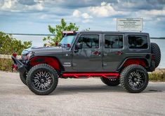 a gray and red jeep is parked by the water