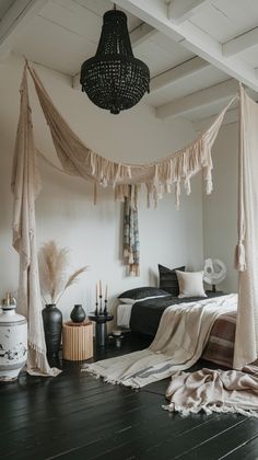 a bedroom with white walls and wooden floors has a canopy over the bed that is draped in tassels