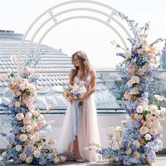 a woman standing in front of an arch with flowers and greenery on the side