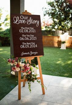 a sign that is sitting on the ground in front of some grass and flowers, with a couple's wedding date written on it