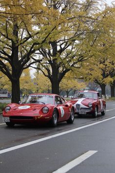 two red sports cars are parked on the side of the road in front of some trees