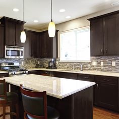 a kitchen with dark wood cabinets and marble counter tops, along with bar stools