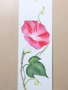 a watercolor painting of a pink flower on a white bookmark with green leaves