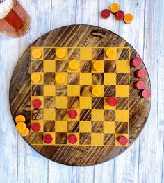 a wooden board with yellow and red chess pieces on it next to a glass of beer