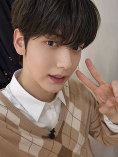 a young man making the peace sign with his hand while wearing a sweater and white shirt