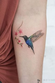 a small hummingbird tattoo on the left upper arm and lower arm, with pink flowers around it