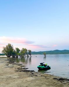 a green jet ski sitting on top of a beach next to the ocean at sunset