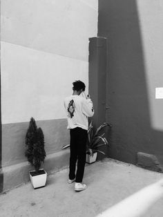 black and white photograph of a person standing next to a wall with potted plants