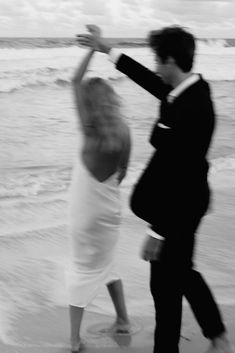 a man and woman are dancing on the beach in front of the ocean while holding hands