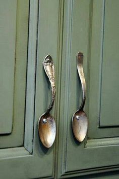 two spoons are hanging on the handles of green cupboard doors, one has a metal handle