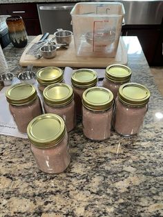 six jars are lined up on the kitchen counter with measuring spoons in front of them