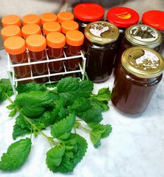 several jars of honey sit on a table next to fresh mint leaves and peppermints