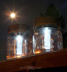 three mason jars with lights in them sitting on top of a wooden shelf at night