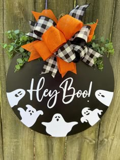 a sign that says hey boo hanging on a fence with pumpkins and ghost decorations