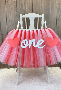 a chair that has some kind of pink tulle with hearts on it and the word one written in white