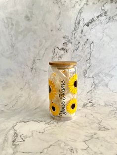 a glass jar with sunflowers on it sitting on a marble countertop next to a wall